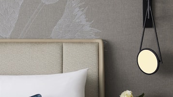 A neatly arranged hotel room with a bed, a bedside table with a vase of flowers, and a wall-mounted lamp.