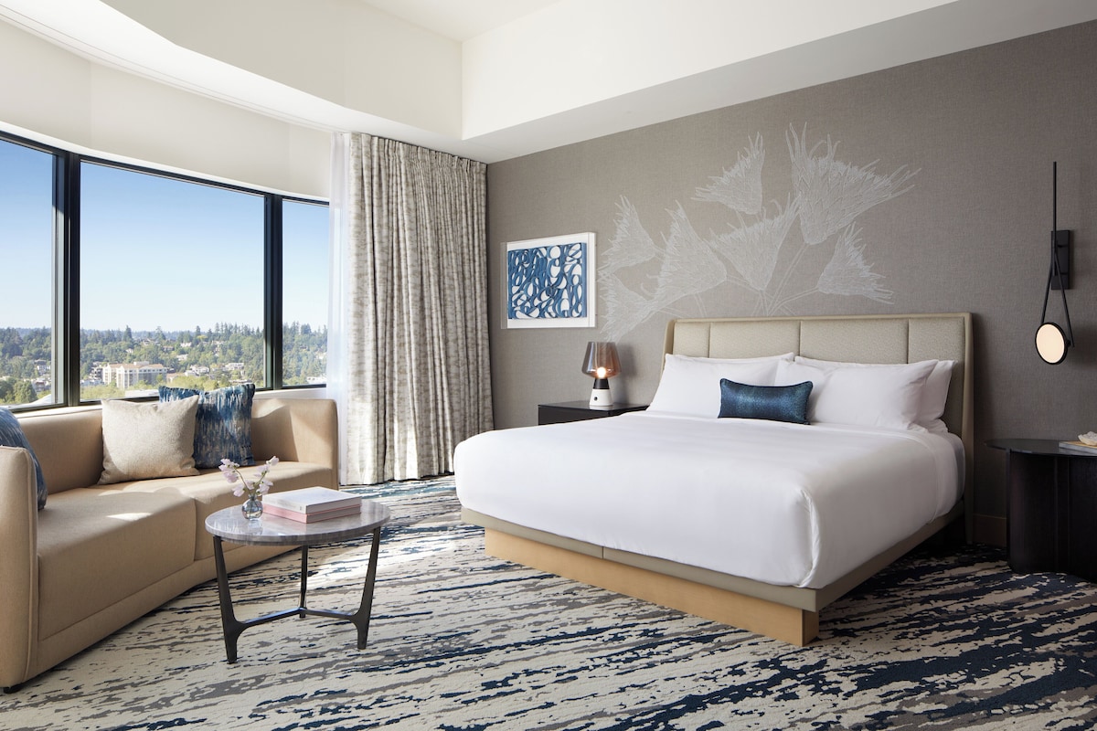 Une chambre d’hôtel moderne avec un grand lit, un canapé, une table basse et une vue sur la ville.