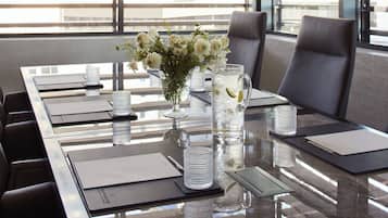 A conference table with a vase of flowers, a pitcher of water with lime, and a glass of water.