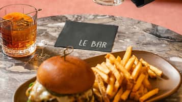 A burger with fries on a plate, a glass of beer, and a menu on a table.