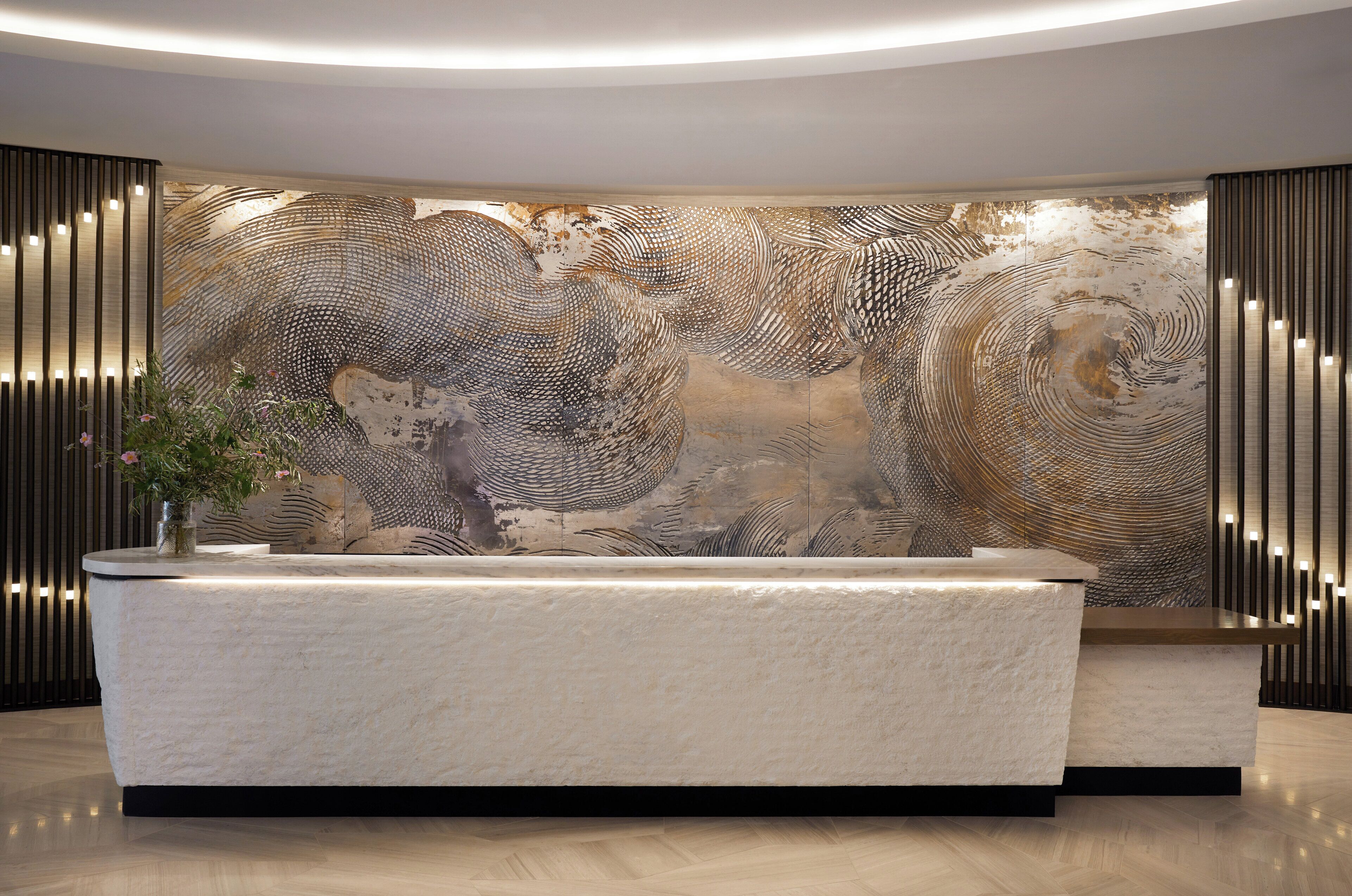 A reception area with a modern reception desk, a large abstract wall art, and vertical light fixtures.