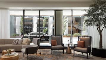 A modern hotel lobby with a large window, a sofa, armchairs, a coffee table, and a potted plant.