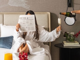 A person reading a newspaper, holding a champagne glass, and another person pouring champagne.