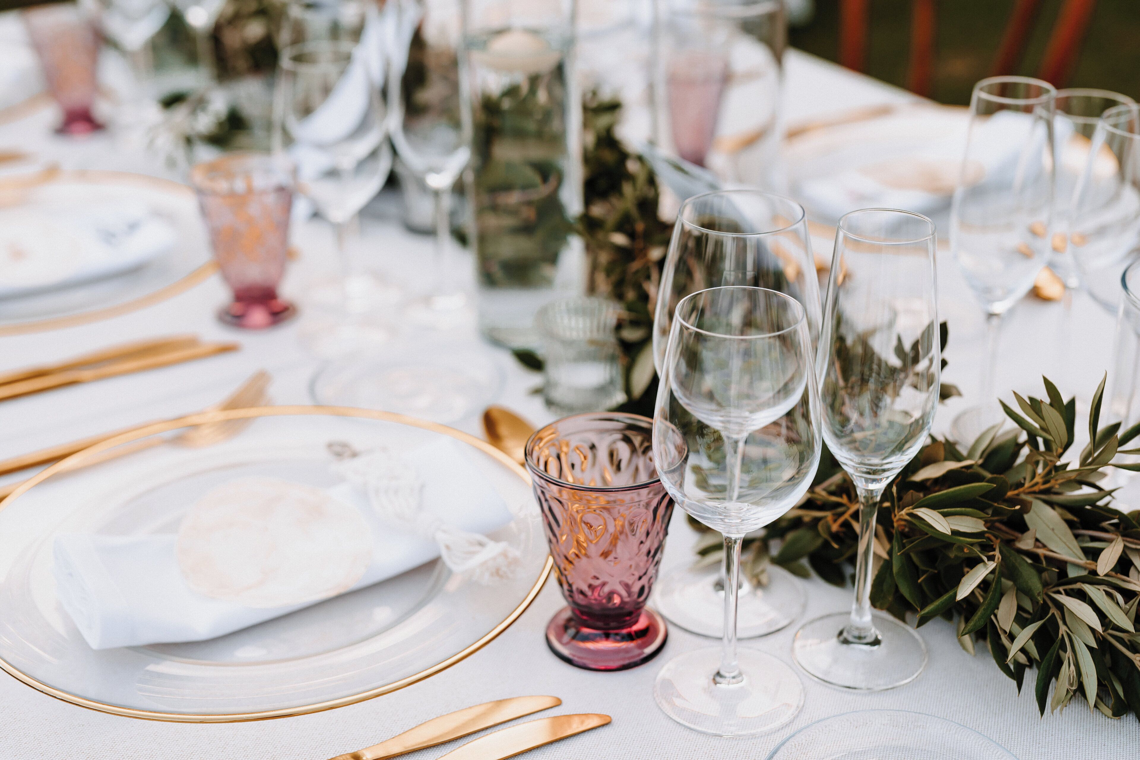 A table set with clear glassware, gold cutlery, and a white tablecloth.