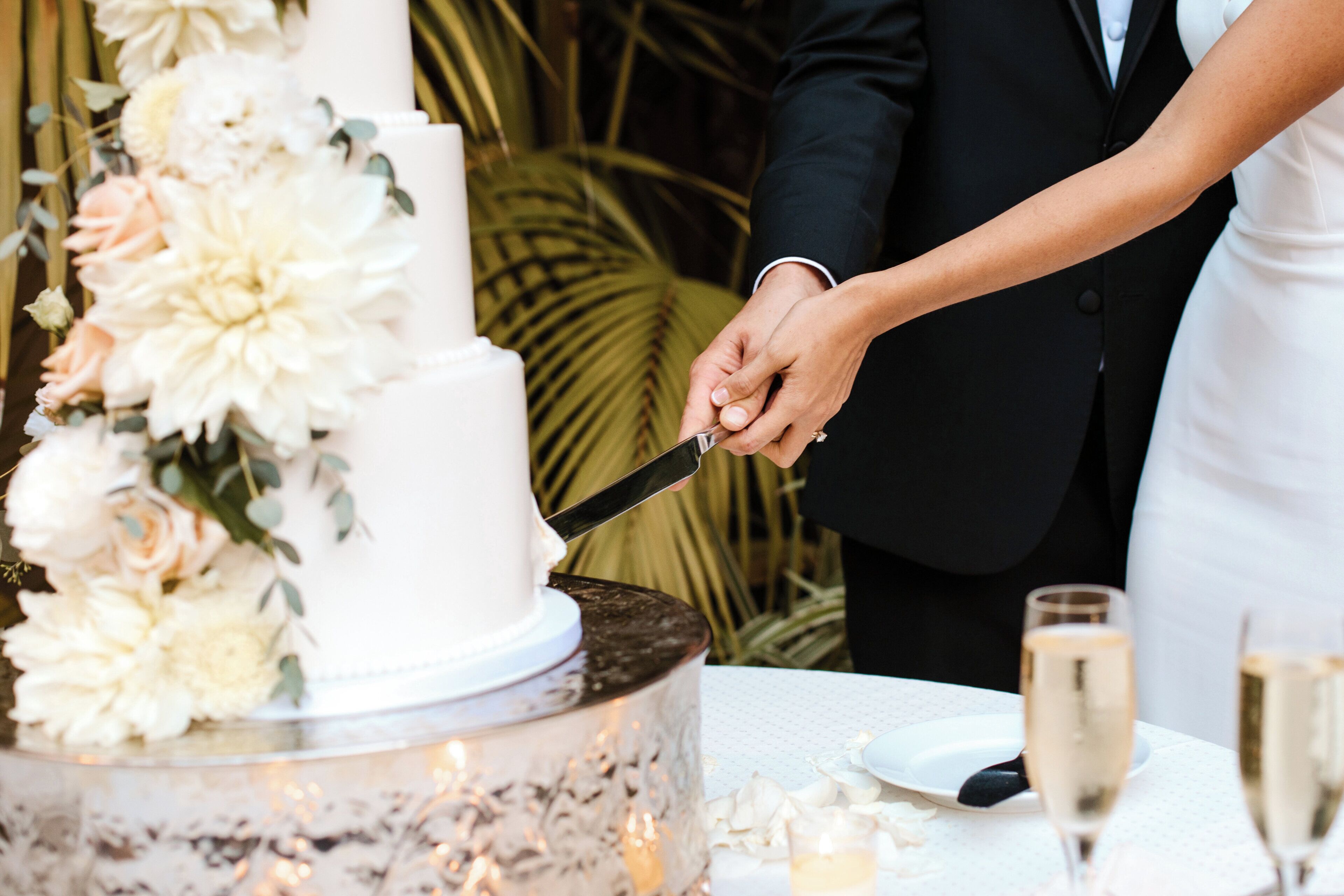 A wedding cake with floral decorations and a couple cutting it.