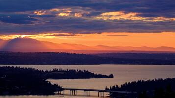A sunset over a body of water with a bridge and distant mountains.