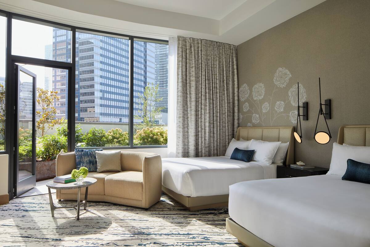 A modern hotel room with a large window, a sofa, a bed, and a small table.