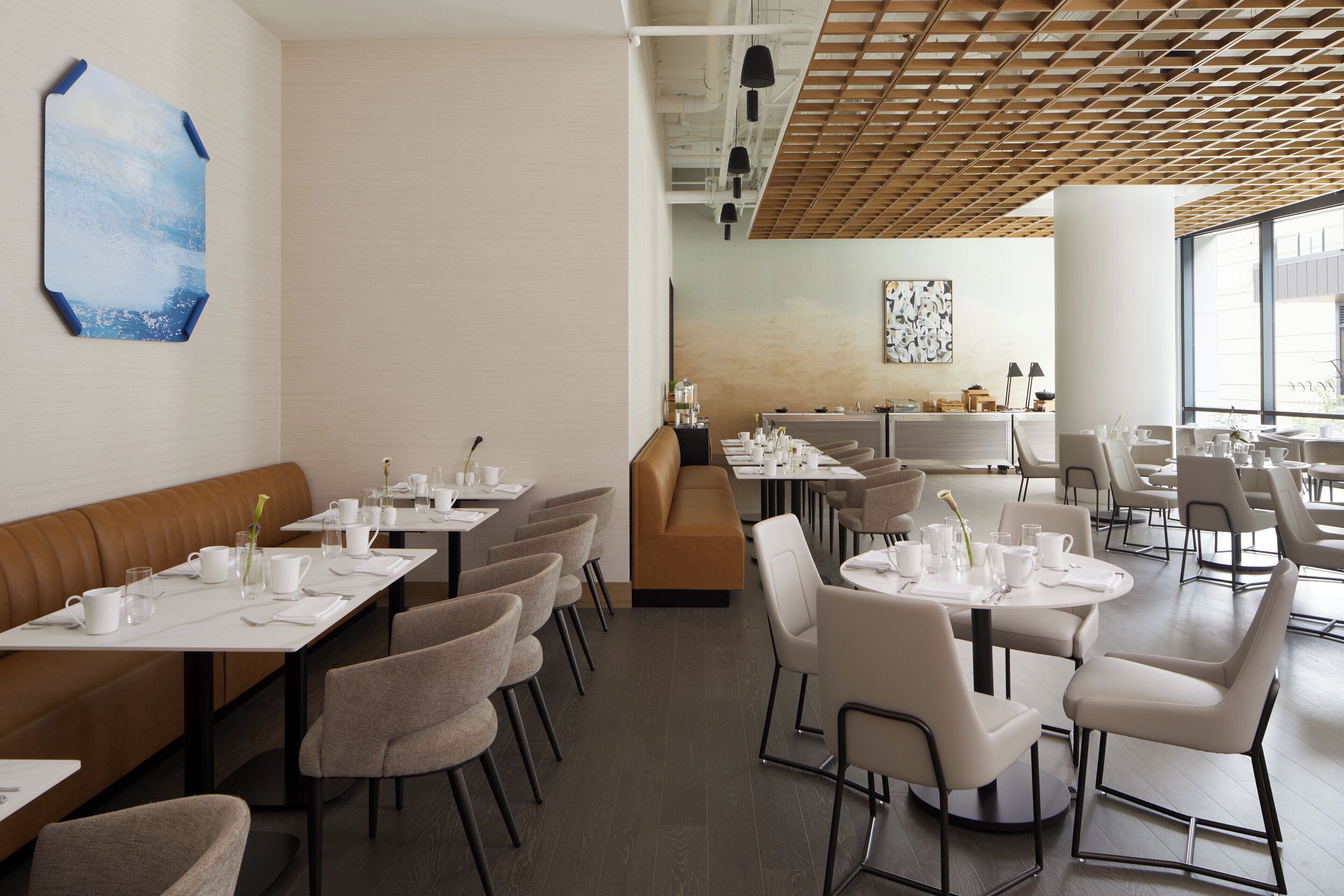 A modern dining area with booths and round tables, featuring a wooden ceiling and large windows.