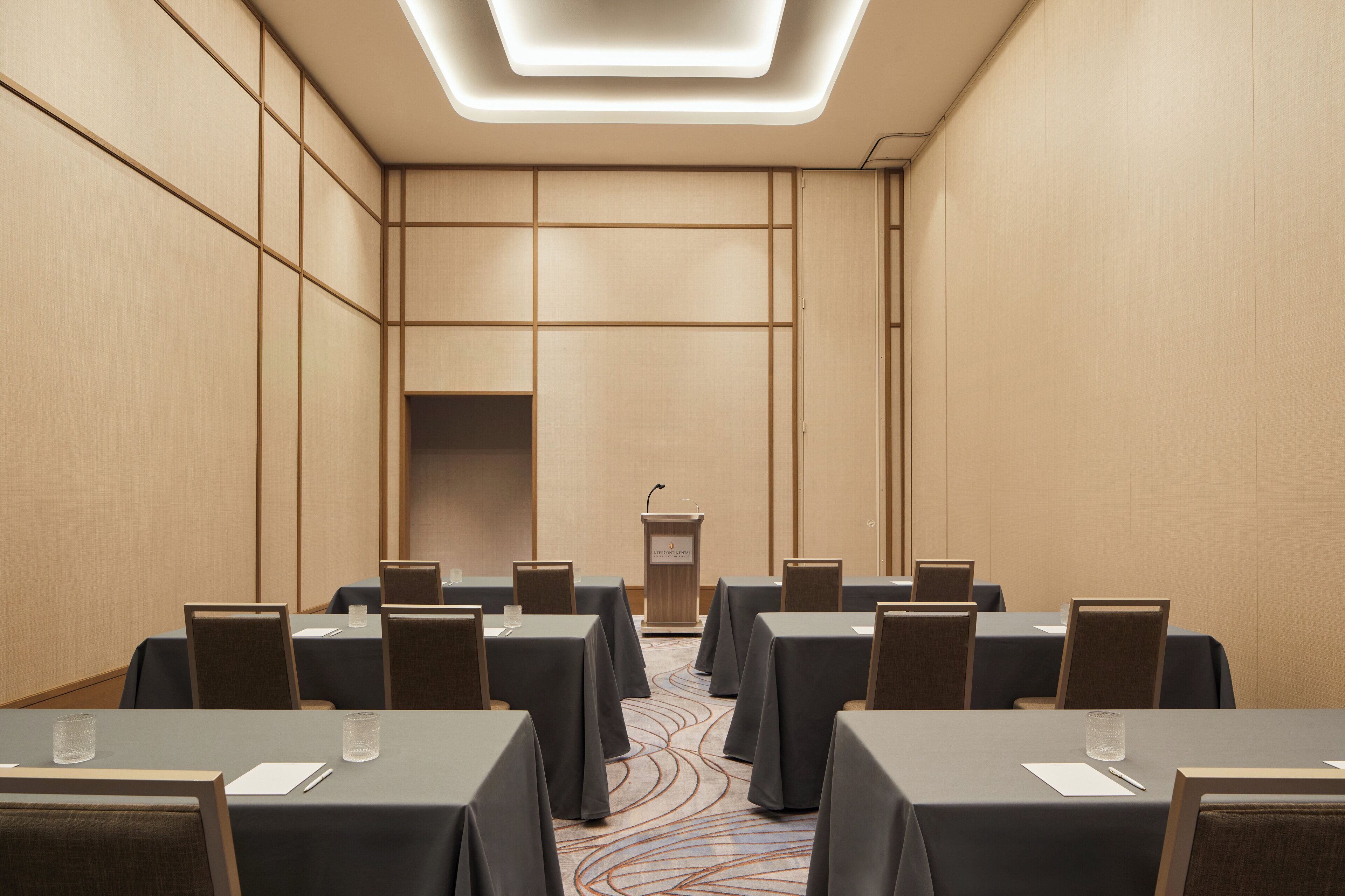 A conference room with tables, chairs, a podium, and a carpeted floor.