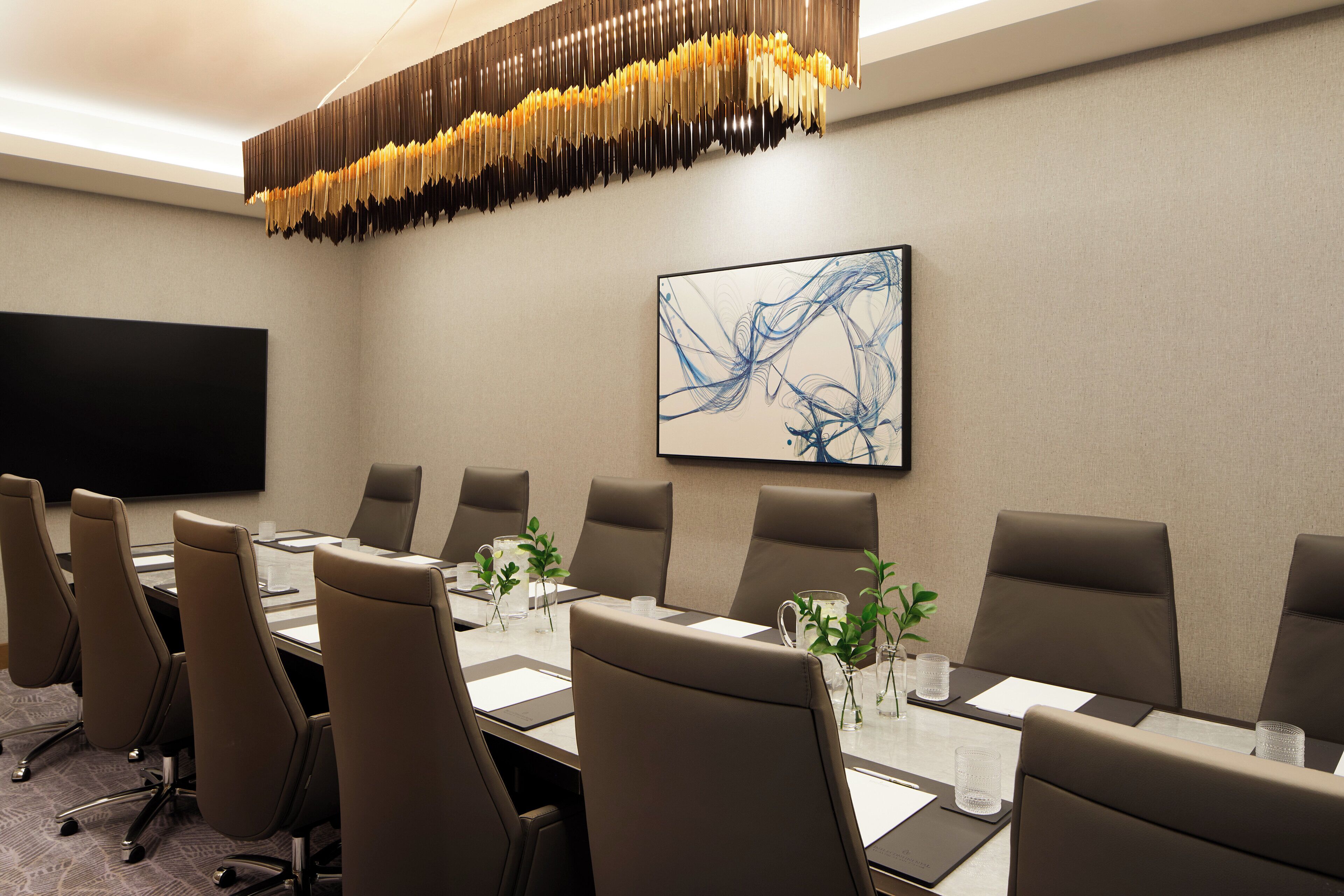 Une salle de conférence avec une longue table, de nombreuses chaises, un téléviseur à écran plat et un tableau moderne représentant une œuvre abstraite accroché au mur.