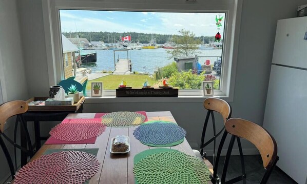 A dining area with a view of a marina and a Canadian flag. - Beautiful Ocean view retreat in Eastern Passage: Serenity by the Ocean 🌊 (Eastern Passage)