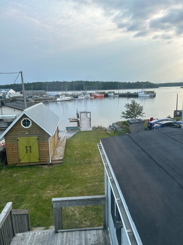 A marina with boats docked, a small wooden building with green doors, and a grassy area with a wooden deck.