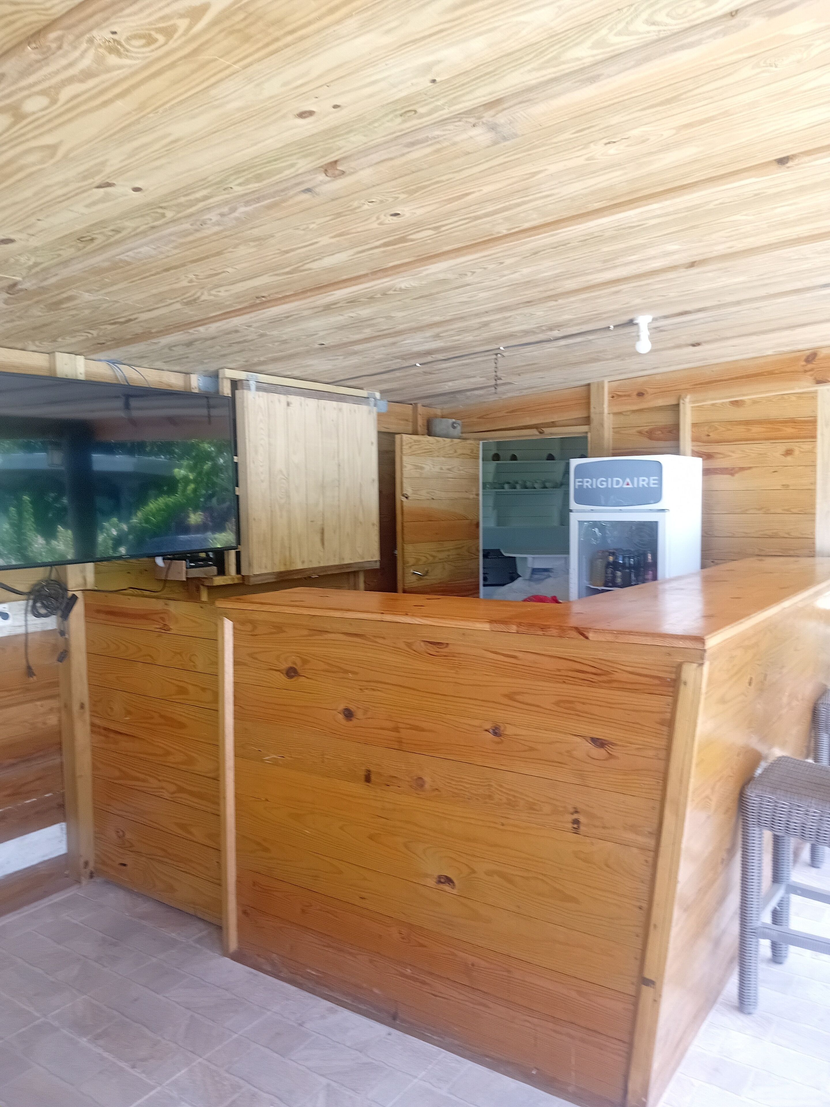 A wooden interior with a kitchen area, including a refrigerator, wooden cabinets, and a television.