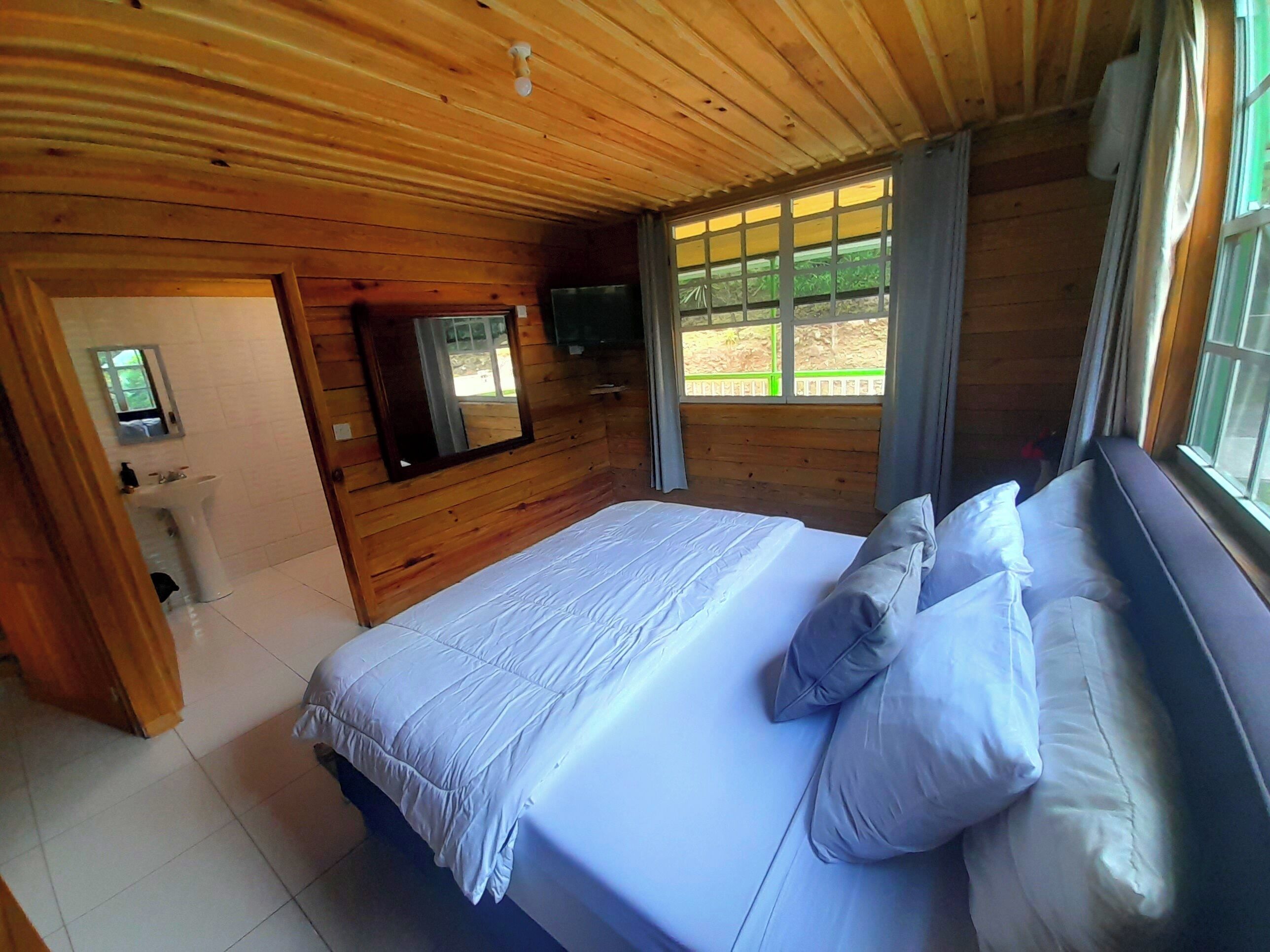 Un dormitorio de cabaña de madera con una cama, un televisor y una ventana con cortinas.