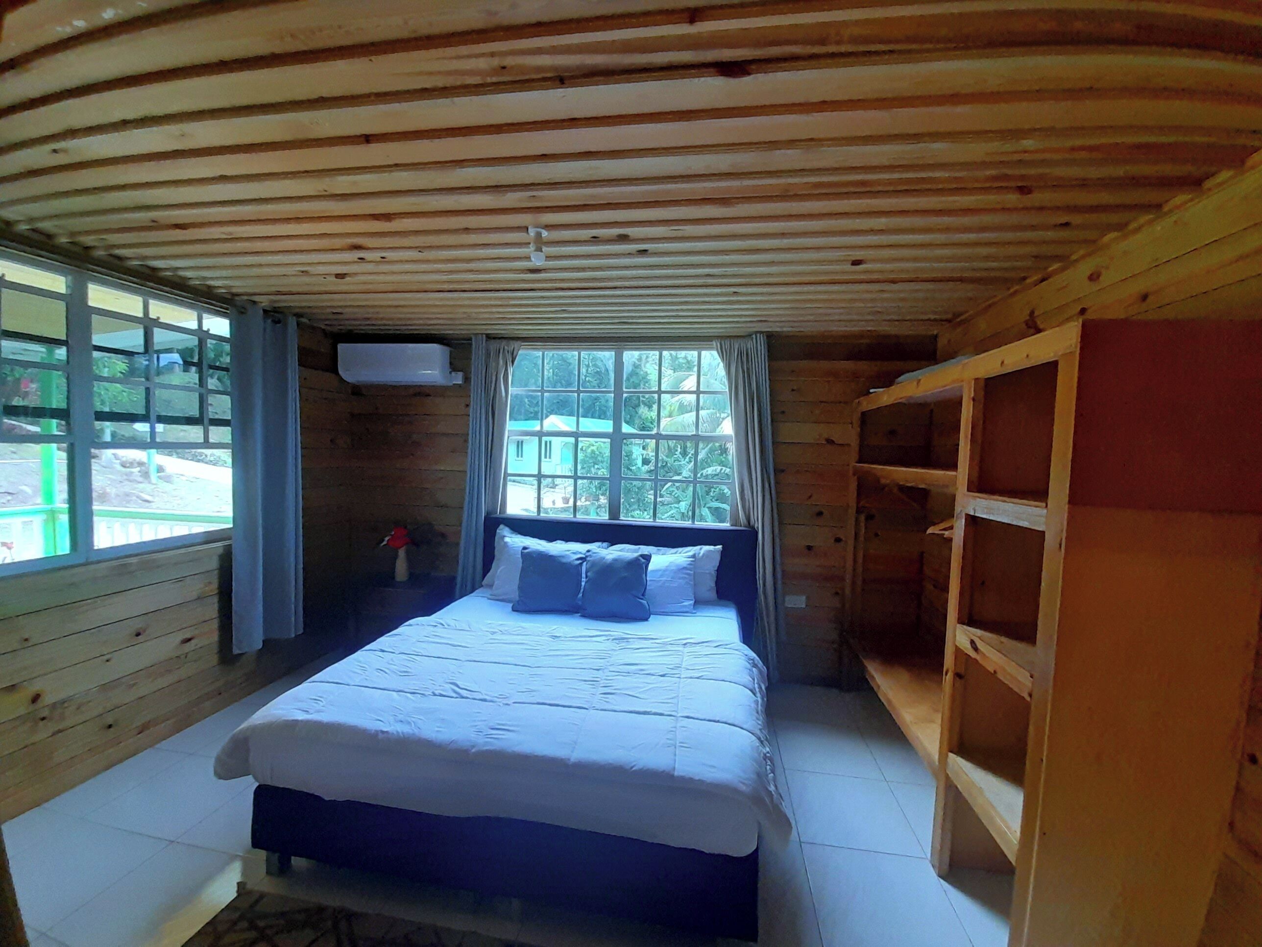A wooden room with a bed, a window, and a built-in shelf.