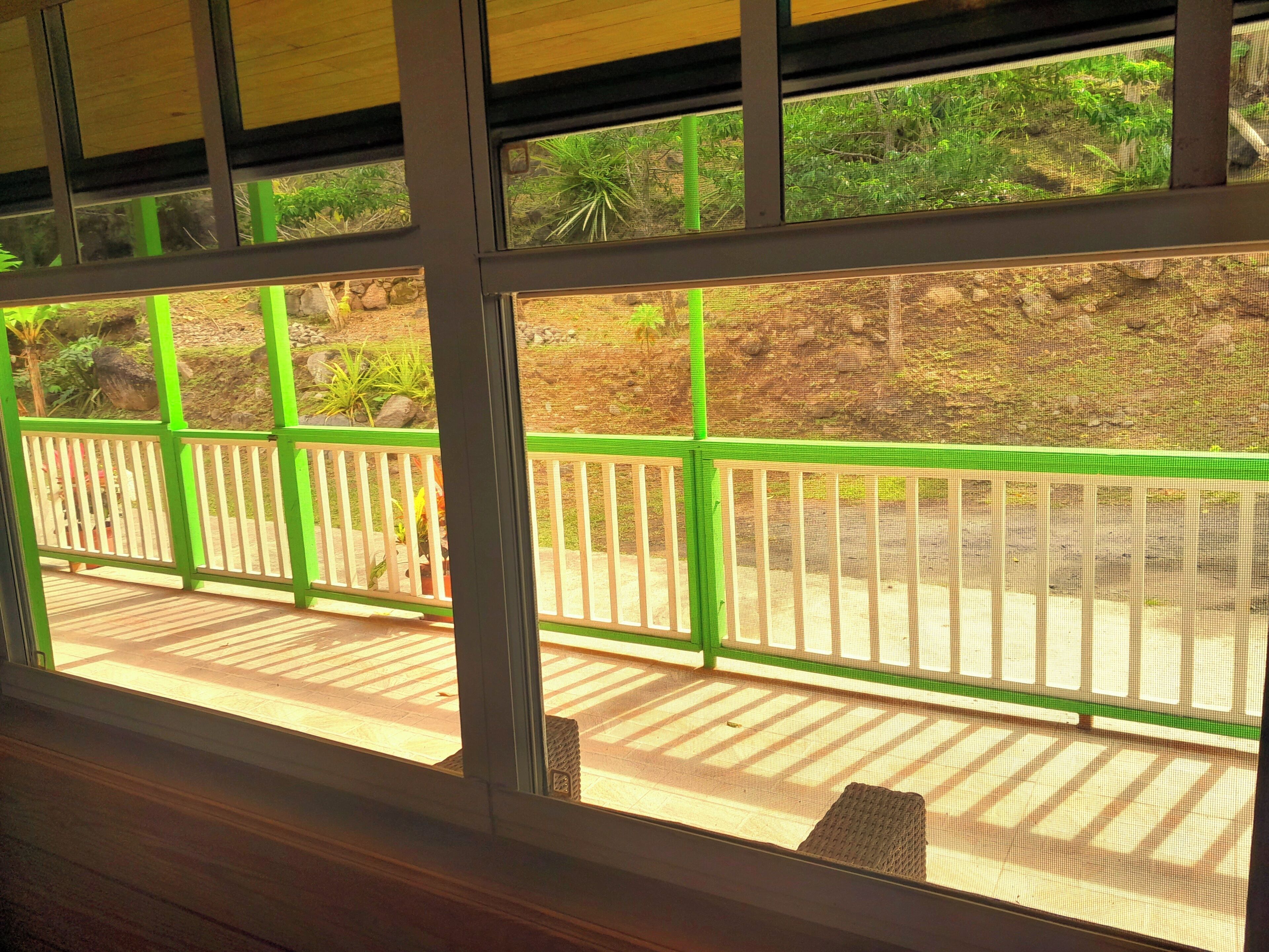 A view through a window with a green railing, a wooden deck, and a rocky landscape outside.