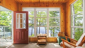 A cabin with a wooden interior, a red door, and large windows overlooking a lake.