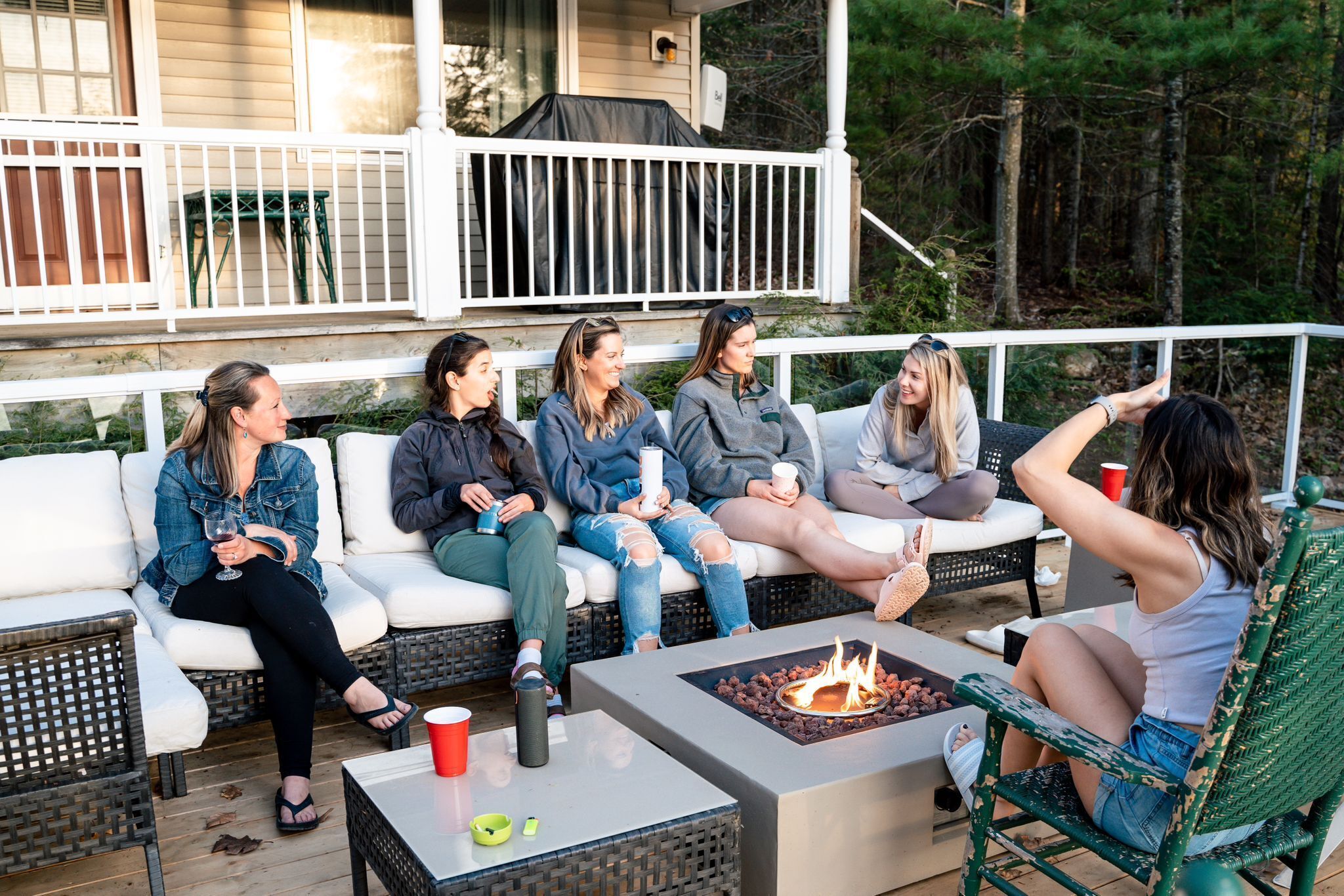 A group of people sitting on a white outdoor deck with a fire pit table in the center.