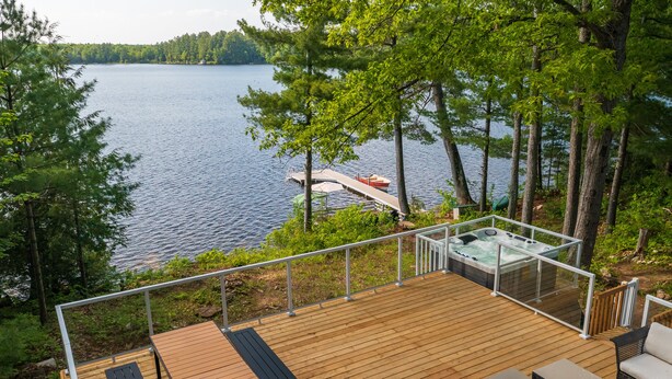 A wooden deck with a hot tub, outdoor seating, and a view of a lake.