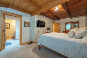 Une chambre avec un plafond en bois, un lit avec une literie blanche, une télévision et un miroir.