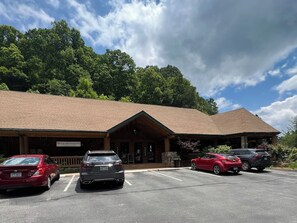 A lodge with a covered entrance, a parking lot with several cars, and a forested backdrop. - Mtn Ski Retreat | Hot Tub + Fire Pit + Fireplace (Mars Hill)