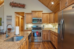 A kitchen with wooden cabinets, stainless steel appliances, and a granite countertop. - Mtn Ski Retreat | Hot Tub + Fire Pit + Fireplace (Mars Hill)