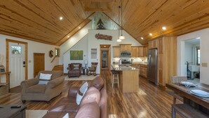 Ein geräumiges Wohnzimmer mit einer großen braunen Ledersofa, Holzboden und einer Küchenzeile mit Holzschränken und Edelstahlgeräten.