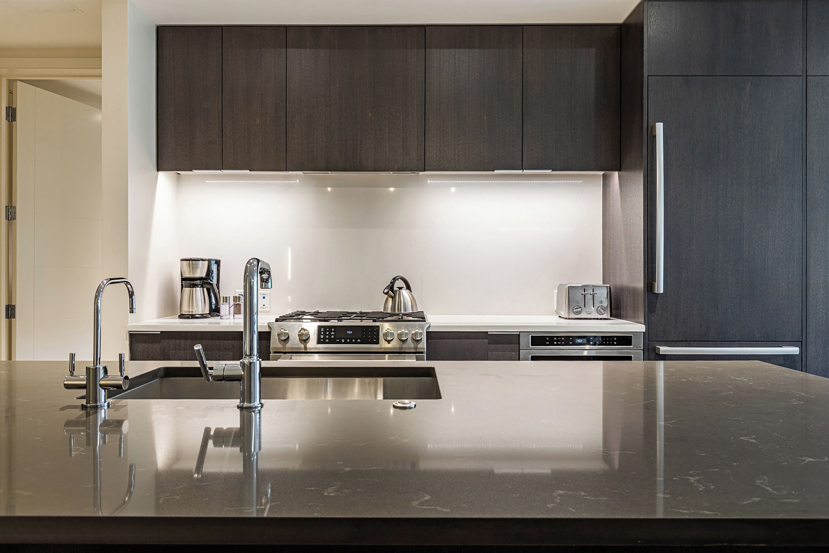 Cozinha moderna com armários escuros, eletrodomésticos de aço inoxidável e bancada elegante.