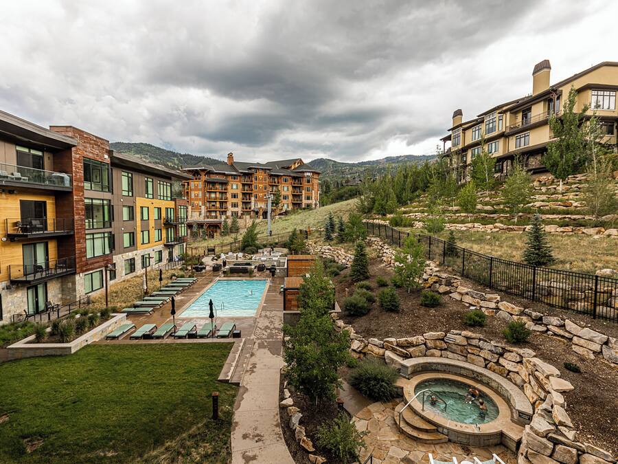A hotel with a swimming pool, outdoor seating, and a view of the mountains.