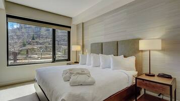 Habitación de hotel con una cama grande, dos lámparas de noche, una mesita de madera y vistas a un paisaje montañoso.
