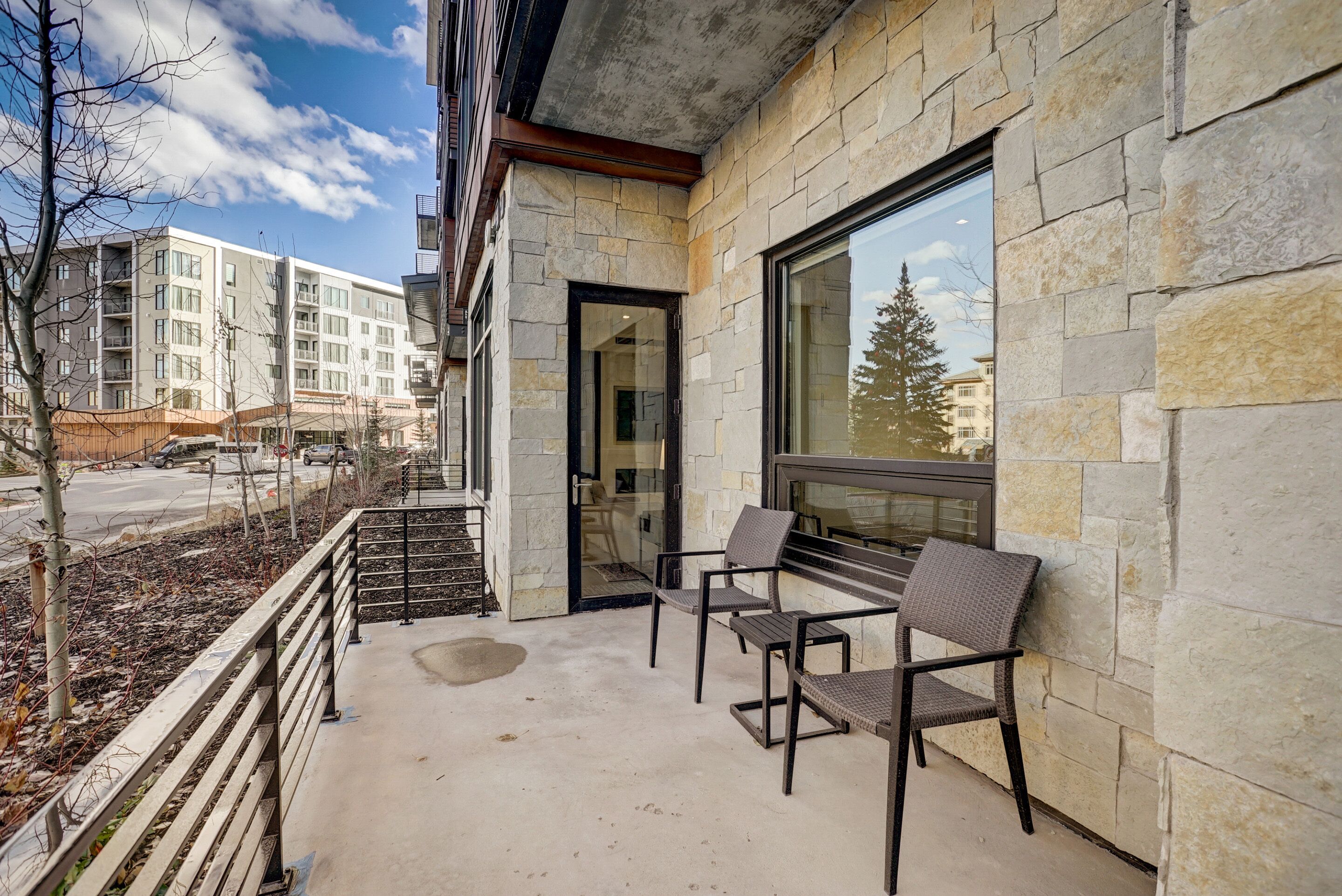 A balcony with stone walls, a glass door, and two wicker chairs.