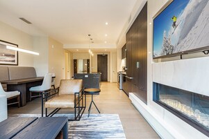 Una sala de estar moderna con chimenea, zona de estar y una cocina al fondo.