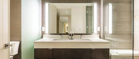 A modern bathroom with a double sink vanity, a large mirror, and a glass shower enclosure.