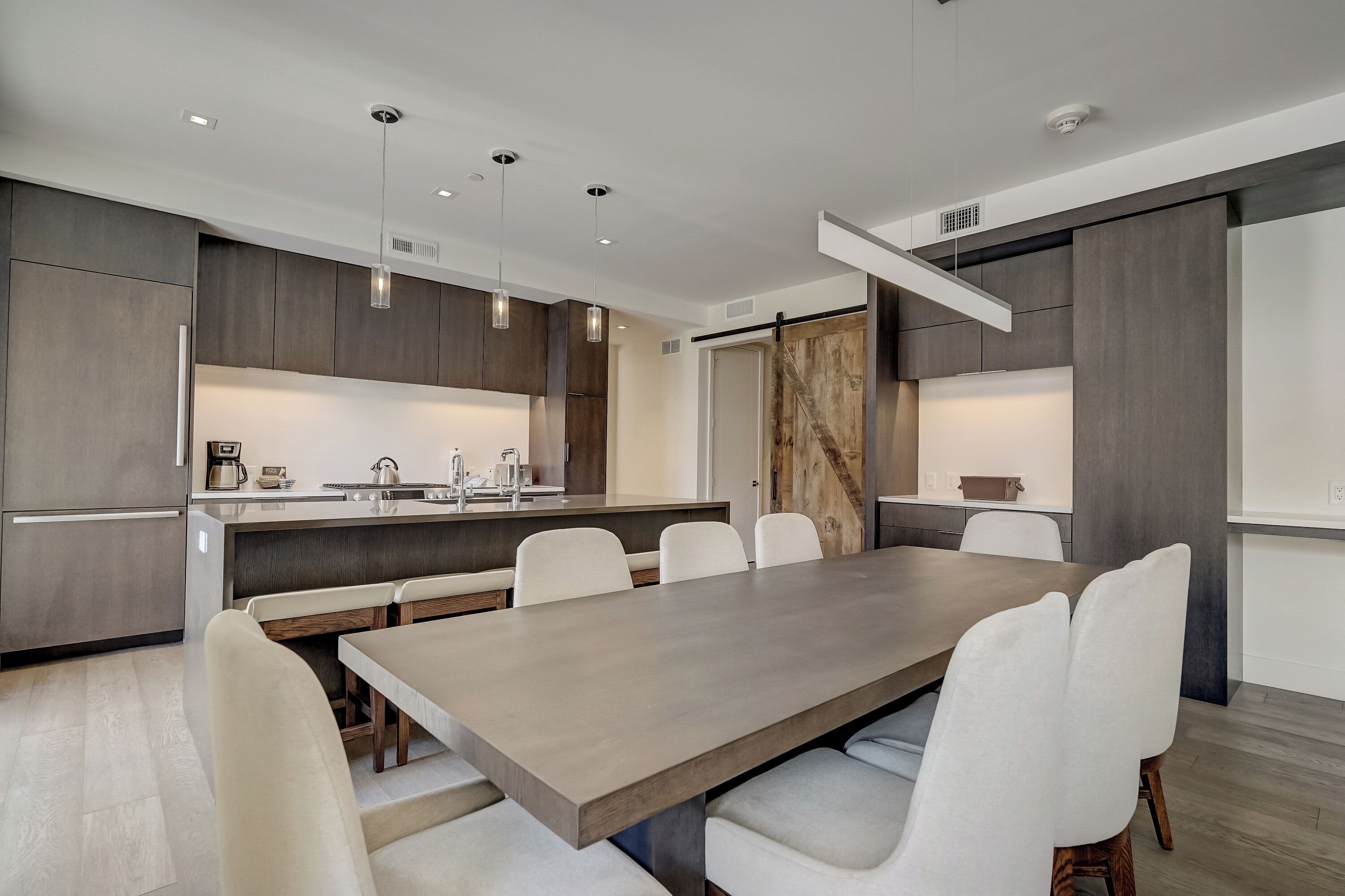 Een moderne keuken met een centraal eiland, witte stoelen en hanglampen.