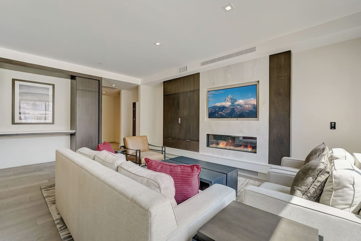 A modern living room with a fireplace, a large TV, and a sofa with cushions.