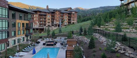 A resort with a swimming pool, lounge chairs, and a view of mountains.