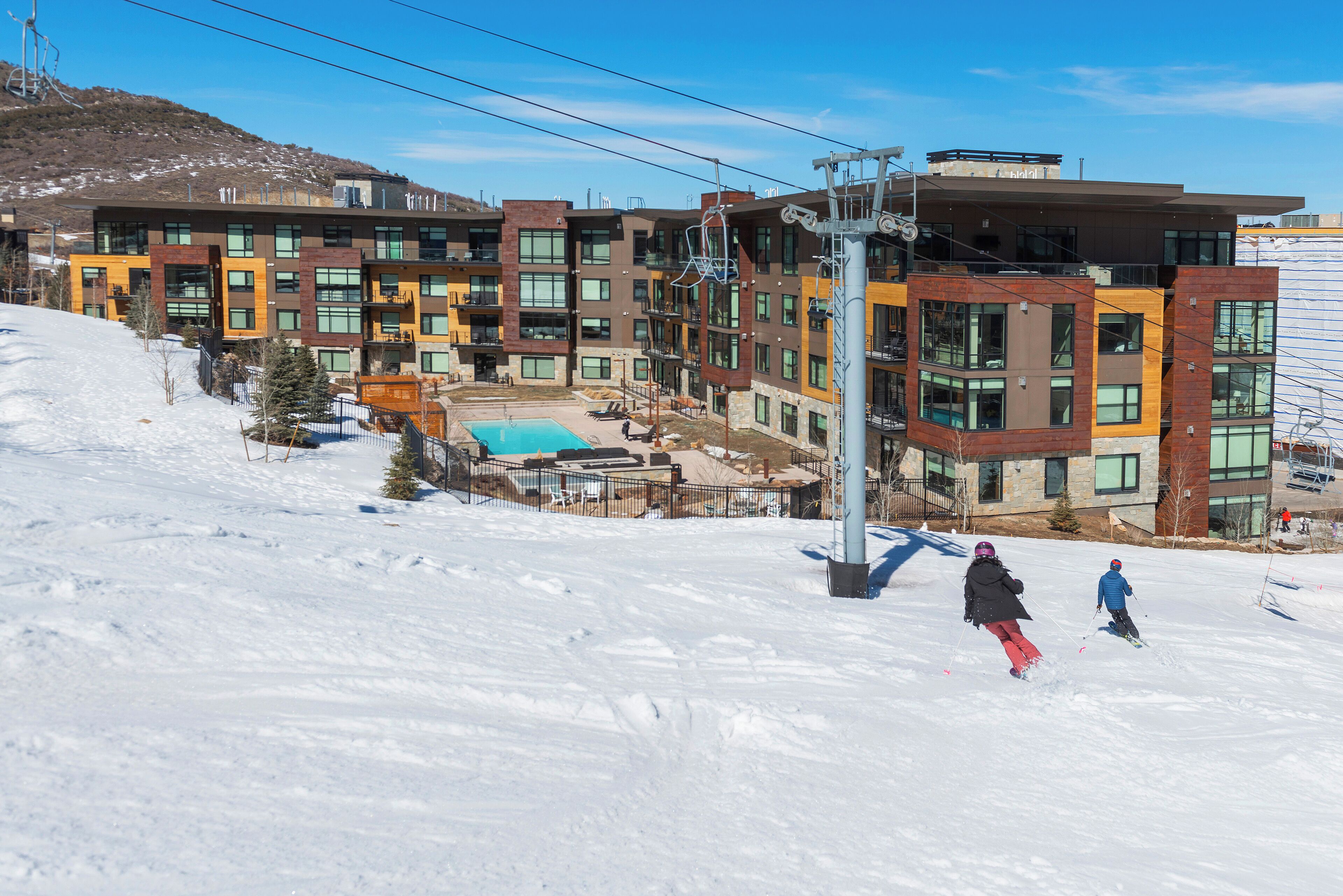 A modern multi-story hotel with a ski slope in the background.