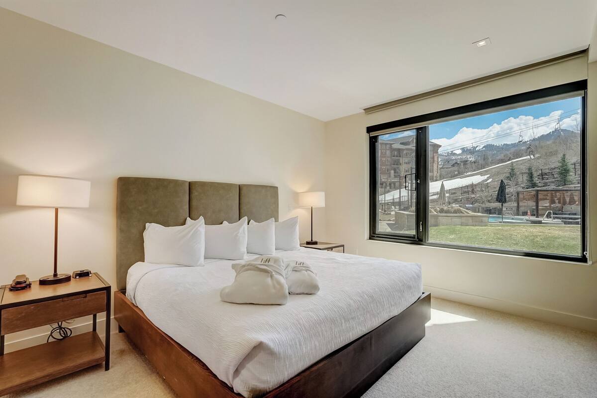 A hotel room with a large bed, two bedside tables, and a view of a ski resort.