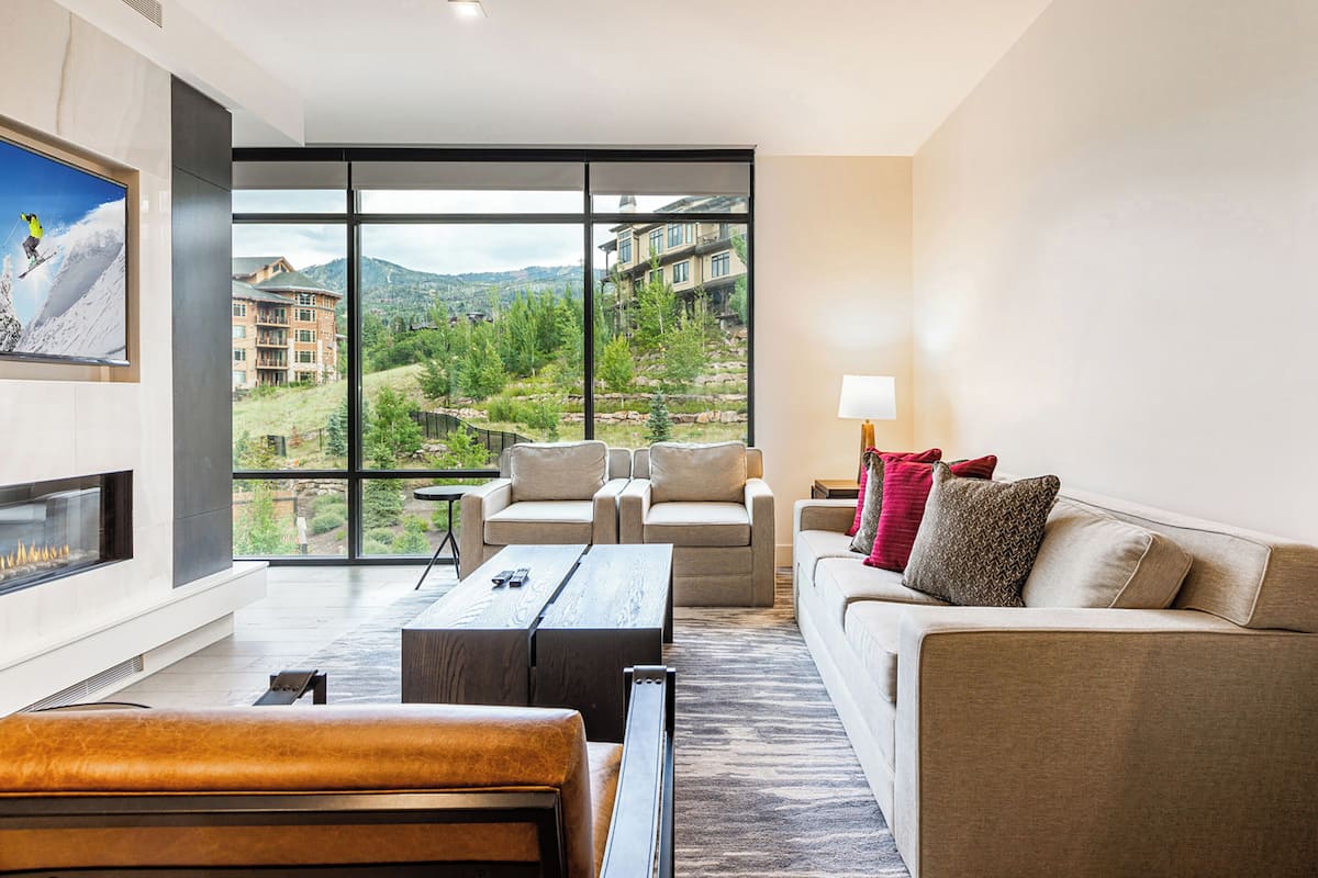 A modern living room with a large window, a fireplace, a sofa, and a coffee table.