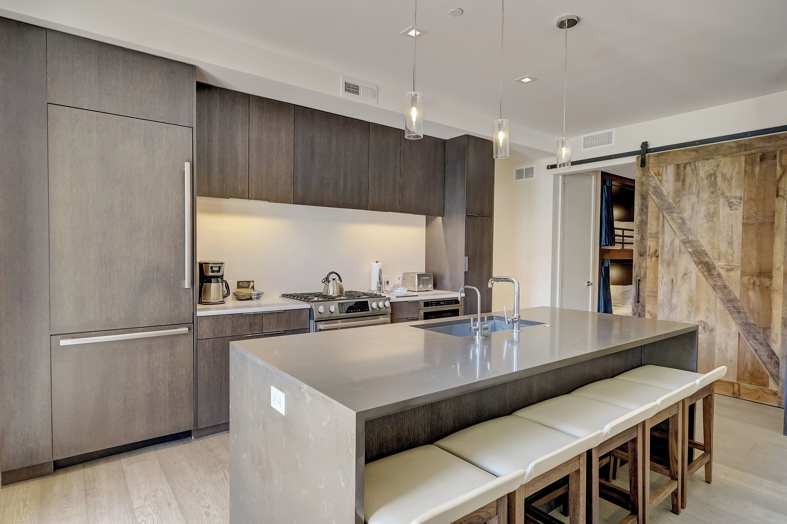 A modern kitchen with a large island, built-in appliances, and a rustic wooden door.