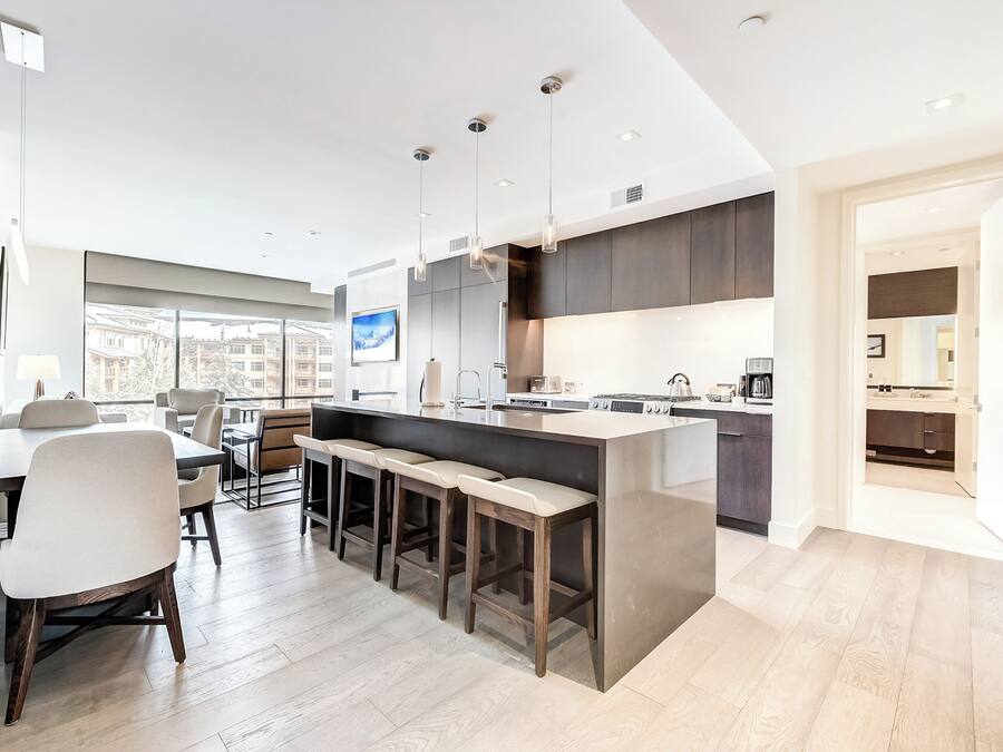 A modern kitchen with a large island, bar stools, and a dining area with a table and chairs.