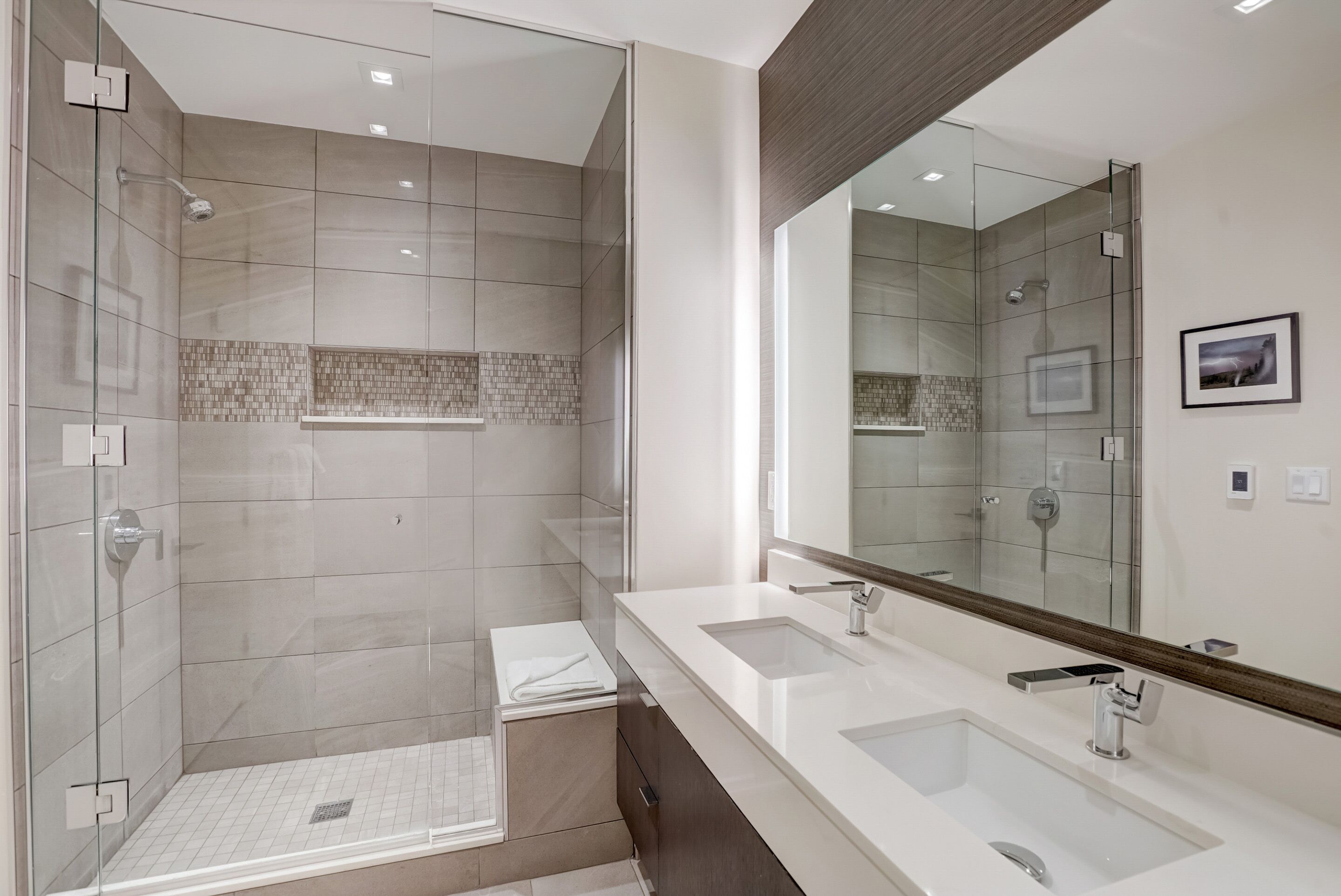 A modern bathroom with a glass-enclosed shower, a large mirror, and a double sink vanity.