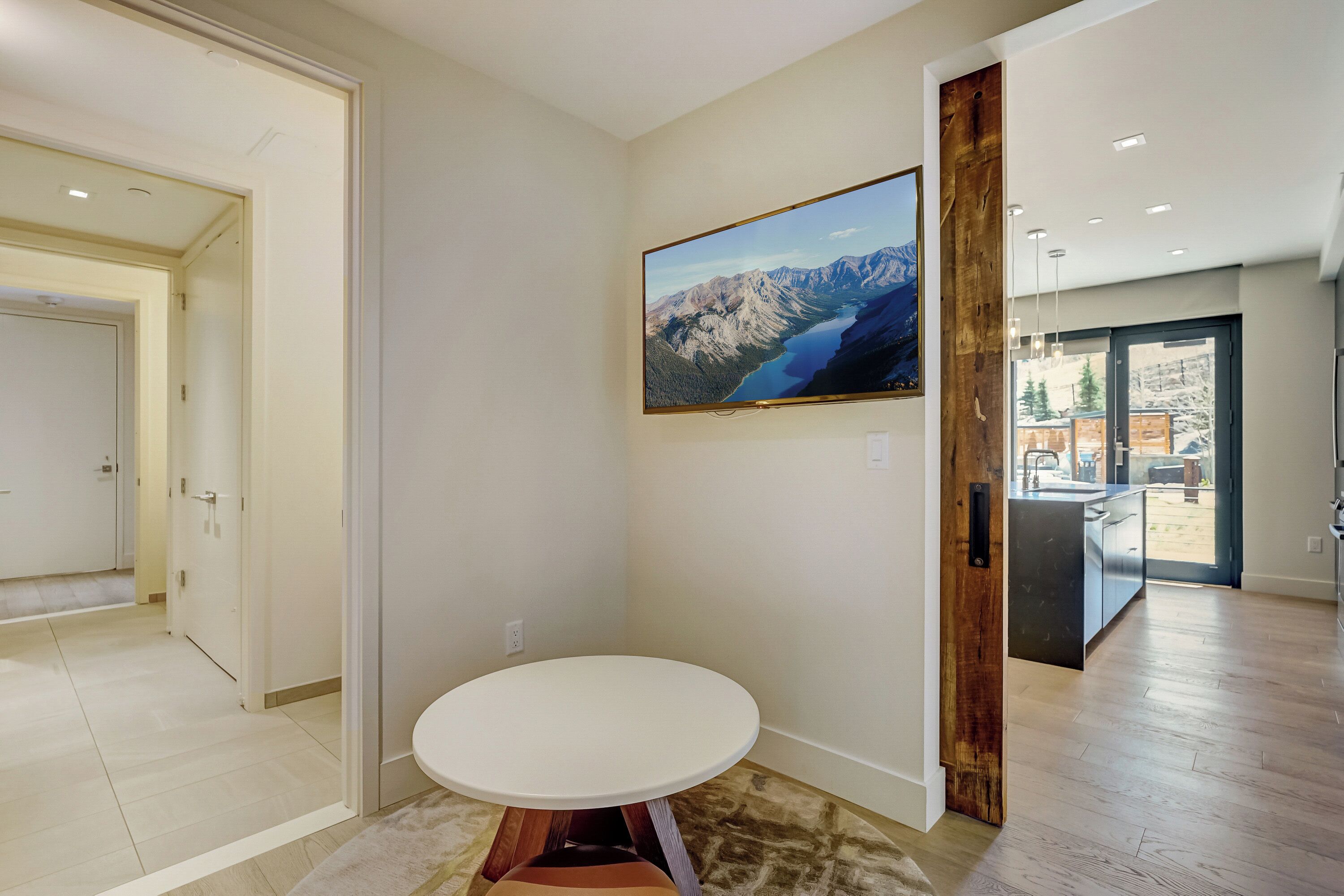 Decoração moderna com uma mesa redonda, uma pintura de paisagem montanhosa e vista para área externa nevada.
