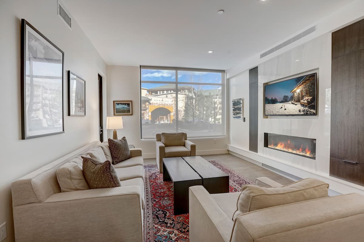A modern living room with a fireplace, large windows, and a cozy seating area.