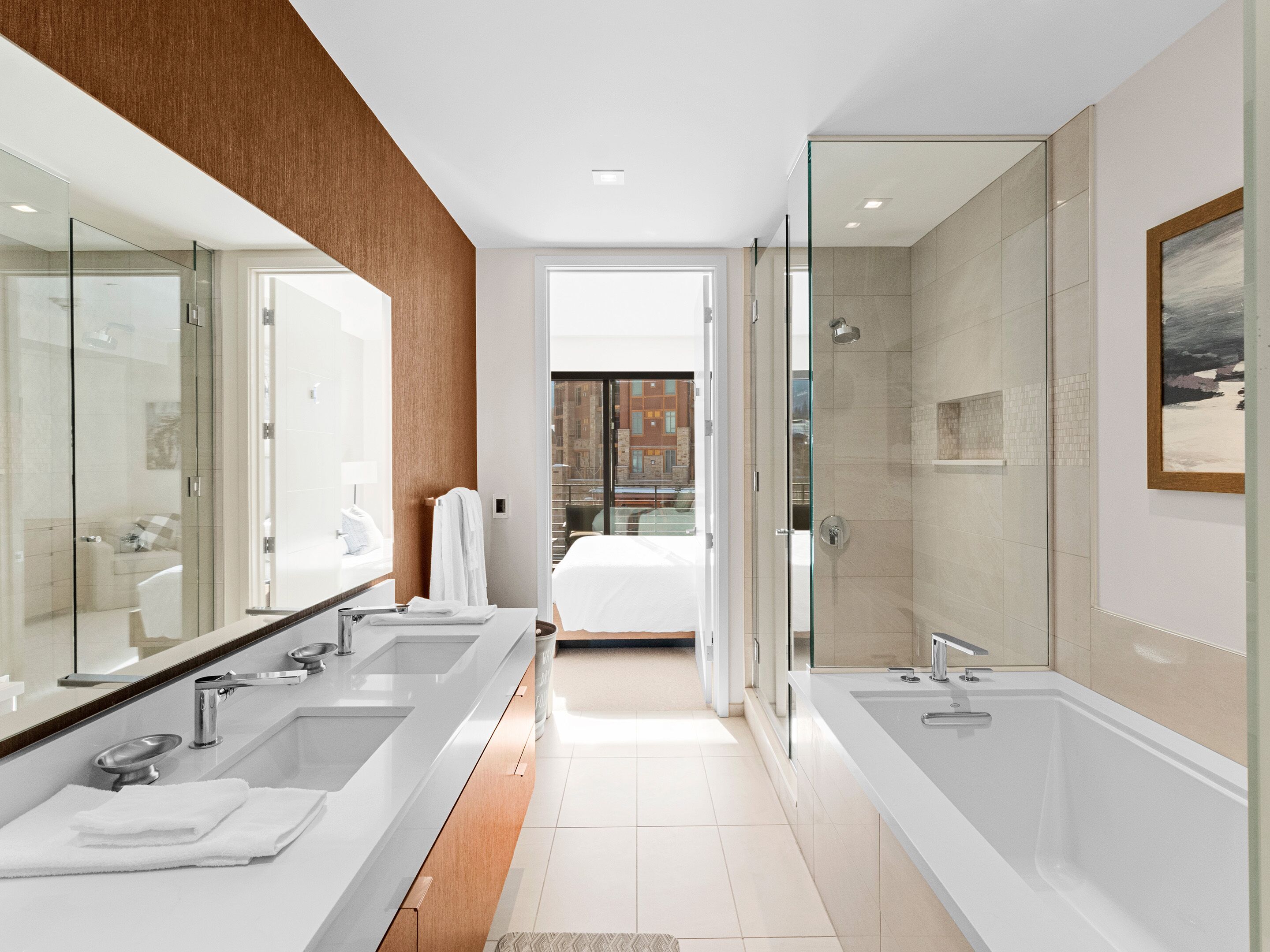 Un baño moderno con lavamanos dobles, un espejo grande y ducha con mampara de vidrio.