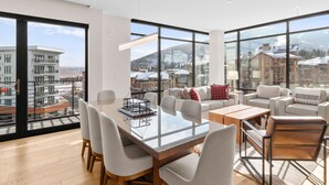 A spacious living area with a large glass table, multiple seating options, and a view of a snowy mountain landscape.