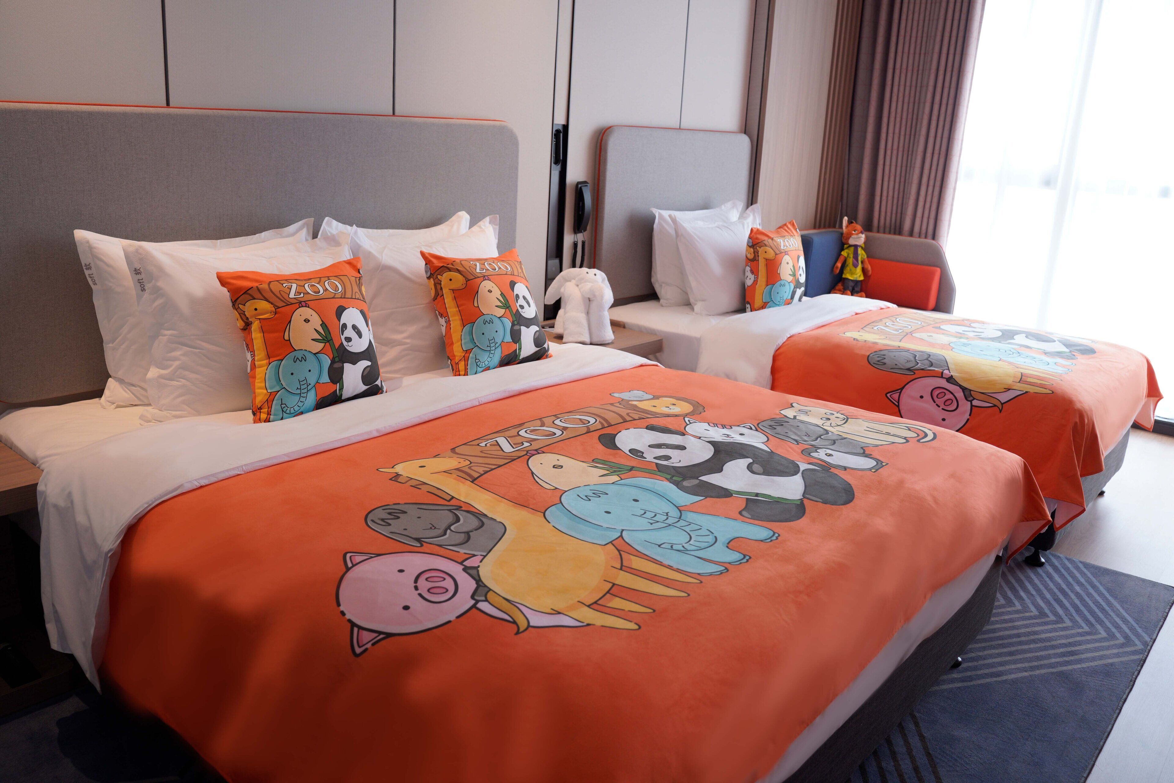 A hotel room with two beds, each with a colorful 'Zoo' themed bedspread and matching pillows.