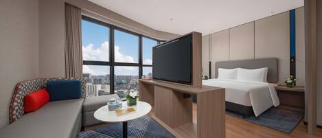 A modern hotel room with a sofa, a bed, a TV, a small table, and a city view.