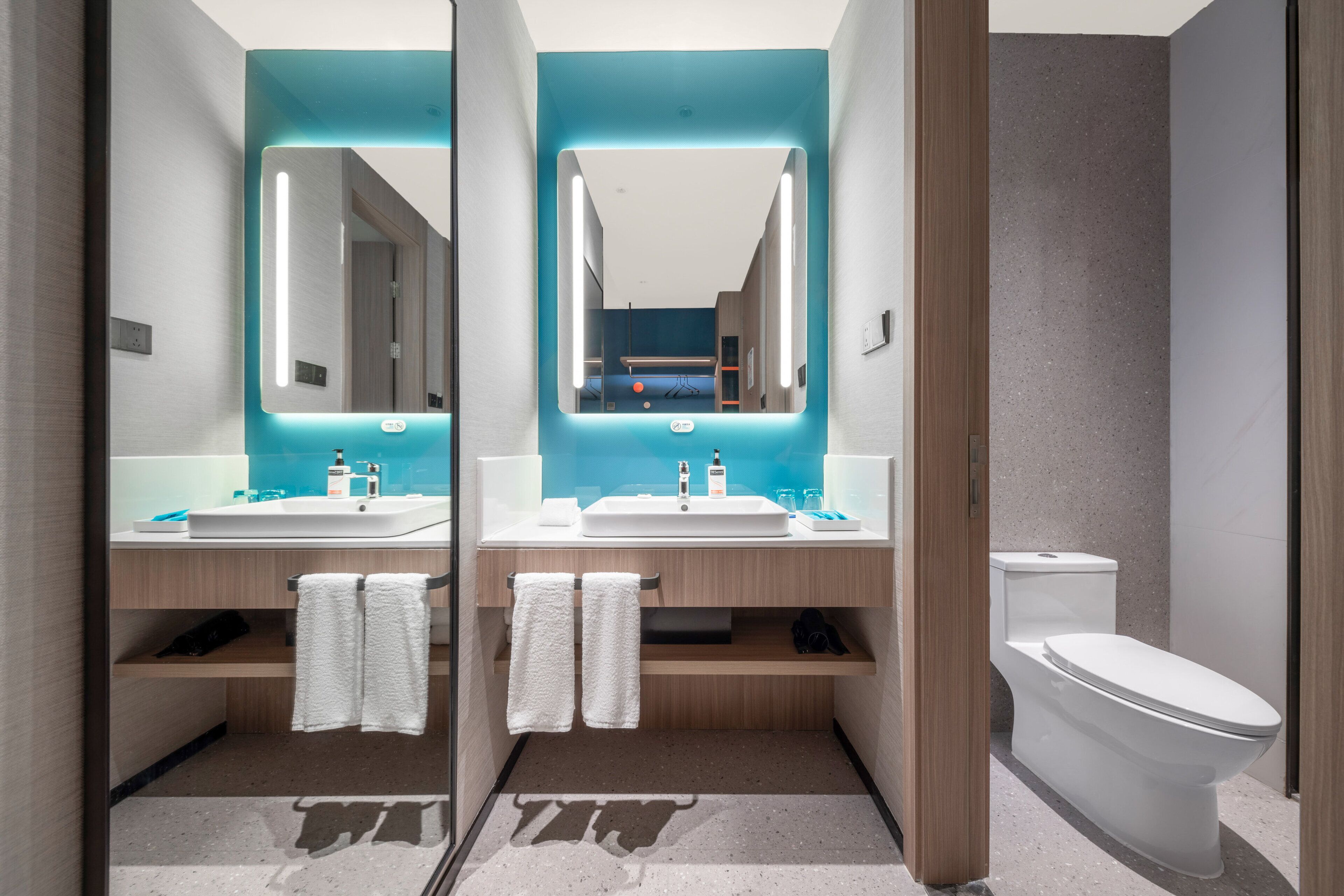 A modern bathroom with two sinks, a toilet, and a mirror with integrated lighting.