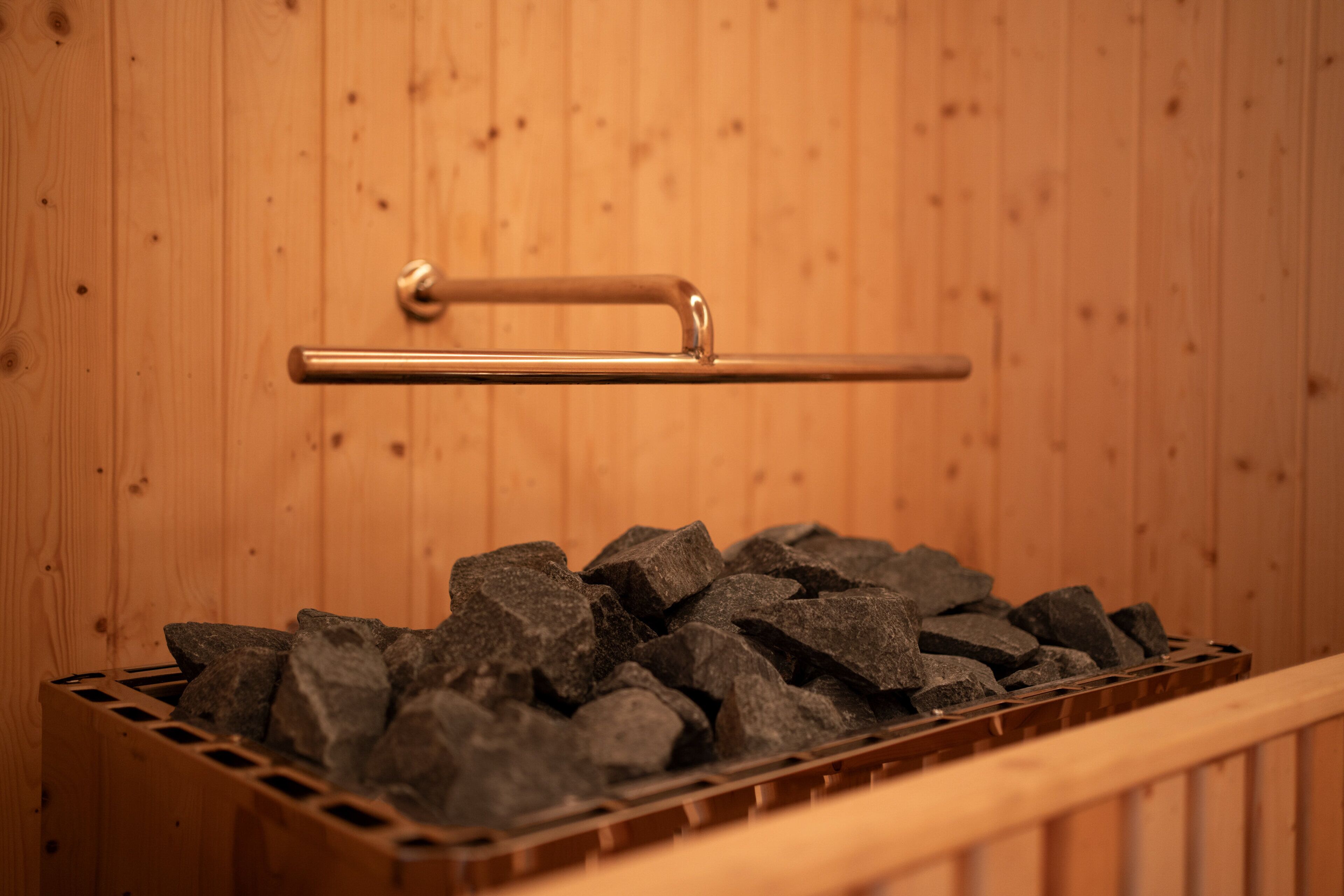 Una sauna de madera con un tirador metálico y un porta rocas de metal.